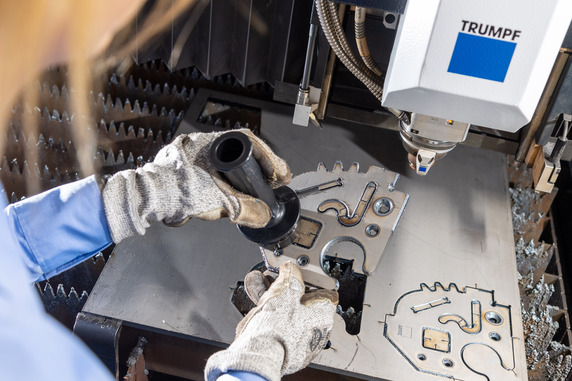 Eine Mitarbeiterin entnimmt ein Bauteil mit Fasen von einer Trumpf Standardmaschine fürs Laserschneiden. © Trumpf / Martin Stollberg